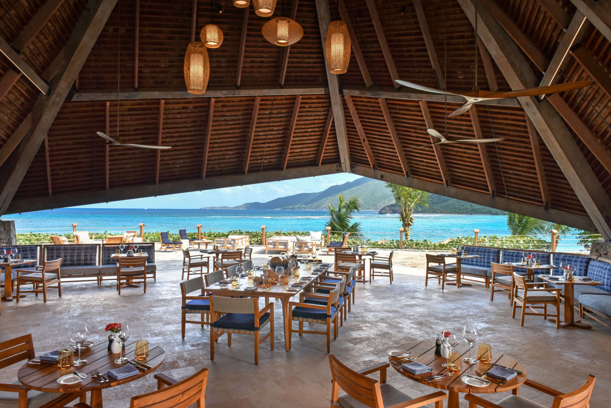 Interior of Rosewood Little Dix Day Pavilion restaurant with empty dining tables and chairs and ocean view